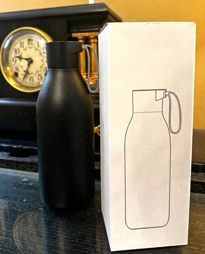 Black insulated bottle next to its packaging box with a line drawing of the bottle on a wooden surface.